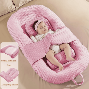 Baby in a pink sleeping lounger nest on a beige surface