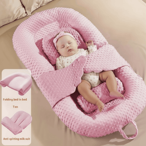 Baby sleeping in a pink baby lounger nest on a bed