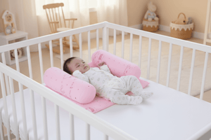Baby lying on a pink pillow in a crib with a soft, neutral-colored room in the background