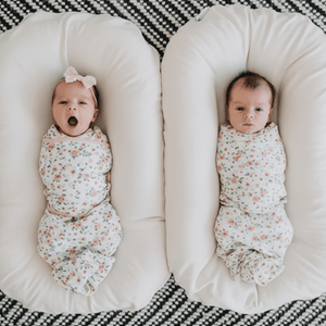 A newborn baby lying in a brown, cushioned baby lounger nest.