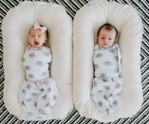 A newborn baby lying in a brown, cushioned baby lounger nest.