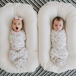 A newborn baby lying in a brown, cushioned baby lounger nest.