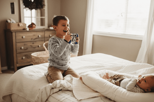 a boy is taking photo of his baby brother from a baby lpounger nest