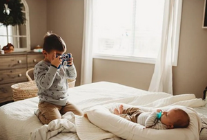 a boy is taking photo of his baby brother from a baby lpounger nest