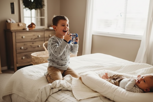 a boy is taking photo of his baby brother from a baby lpounger nest
