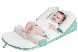 A baby lying on a green and white anti-reflux and anti-roll baby lounger bed.