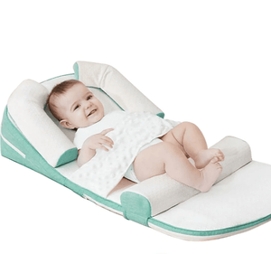 A baby lying on a green and white anti-reflux and anti-roll baby lounger bed.