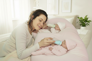 Two babies lying on a pink cushion, being fed with bottles.