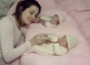 Woman feeding two babies with bottles on a pink blanket