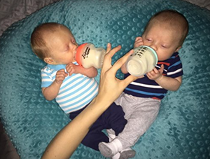 Two babies drinking from bottles on a teal textured surface.