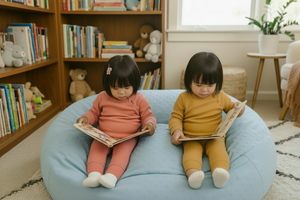 Two children sitting on a blue cushion, each reading a book in a nursery setting.