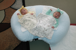 Two babies swaddled in wraps lying on a blue cushioned surface.