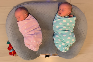 Two babies wrapped in Star Wars-themed blankets on a teal cushion.