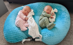 Two babies sleeping on a blue bean bag with white and blue blankets.