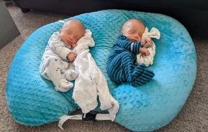 Two babies sleeping on a blue bean bag with white and blue blankets.