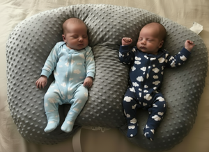 Two babies in patterned onesies lying on a gray pillow.