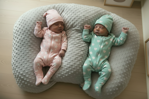 Two babies in matching outfits lying on a gray pillow.