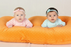 Two babies lying on a yellow blanket wearing pink outfits and headbands.