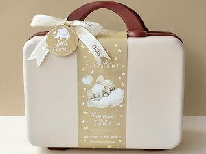 White baby suitcase with brown handle and decorative label on a beige background