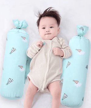Baby lying between two light blue pillows with cloud patterns on a white background