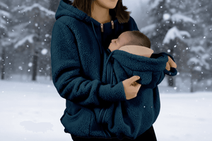 Person wearing a blue fleece jacket holding a baby in a snowy landscape with a flame graphic at the bottom right corner.