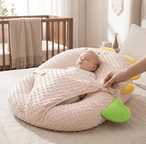 Baby sleeping in a pink cushioned nest with a green toy, in a softly lit room.