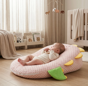 Baby lying on a pink cushion in a nursery with a crib and mobile in the background.