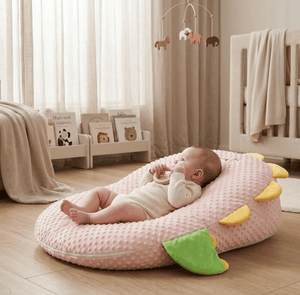 Baby lying on a pink cushion in a nursery with a crib and mobile in the background.