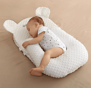 Baby sleeping on a white pillow with bear ears on a beige surface