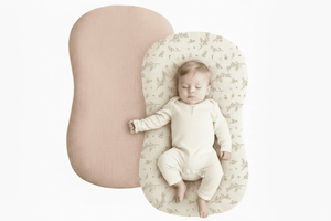 Baby lying on a floral-patterned cushion next to a pink cushion on a white background