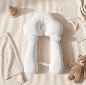 White baby support pillow on a textured beige surface with toys and blankets.