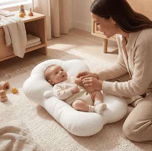 Woman sitting on the floor with a baby in a white baby seat in a bright room.