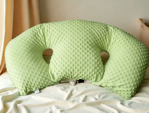 Green U-shaped pillow on a bed with a neutral background