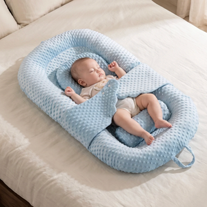 Baby sleeping in a blue woven baby nest on a bed.