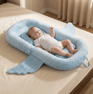 Baby lying in a blue U-shaped pillow on a bed.