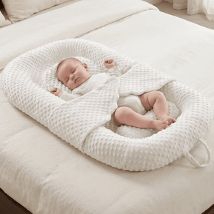 Baby sleeping in a white textured nest on a bed