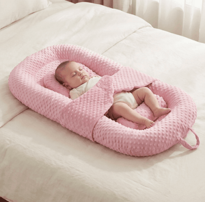 Baby sleeping in a pink baby nest on a white bed