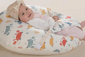 Baby lying on a wedge-shaped pillow with a 15-degree angle, wearing a patterned outfit and headband.