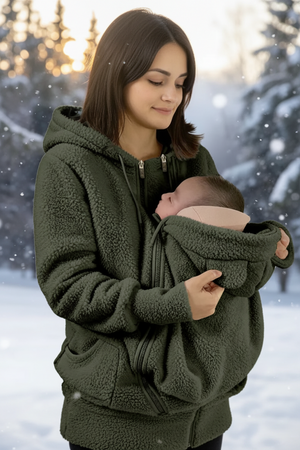 A woman wearing an olive green fleece hoodie with a built-in baby carrier pocket holding a baby, set against a snowy outdoor background with a flame graphic indicating warmth.