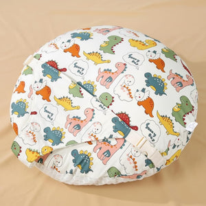 A round baby blanket or cushion cover featuring a colorful cartoon dinosaur pattern on a white background, displayed on a beige fabric surface