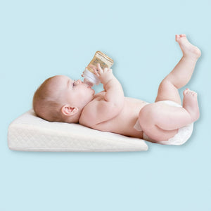 An infant lying on a white DreamLift Anti-Reflux Infant Wedge Pillow while drinking from a bottle.