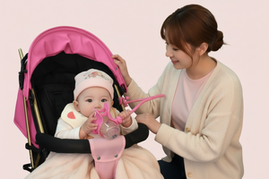 Woman holding a baby in a pink stroller against a light pink background