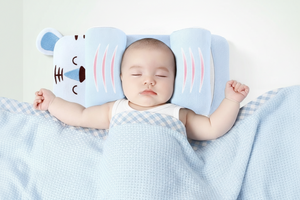 Baby sleeping with a blue pillow shaped like a cartoon character on a white background
