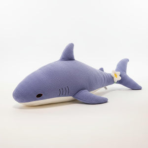 Blue shark-shaped pillow on a bed with a wooden headboard and decorative items in the background.