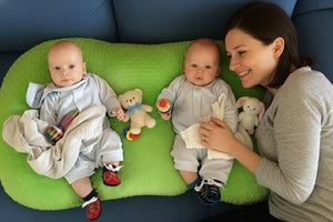Two babies lying on a green mat with toys around them.