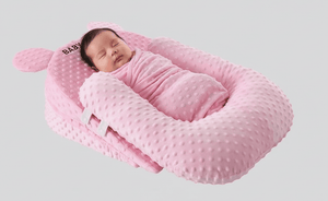 Newborn baby sleeping in a pink minky dot baby nest on a light gray background
