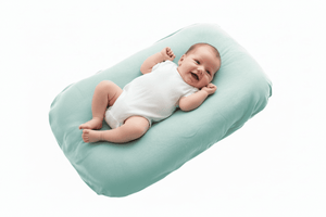 Baby lying on a light green baby lounger nest baby pillow against a white background