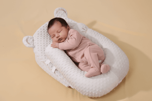 Newborn baby in a pink outfit sleeping in a white crib on a beige background