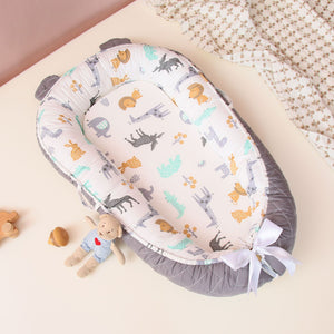 A Cuddle Newborn Baby Lounger with a pattern of animals and leaves on a gray background, displayed with a small toy beside it.
