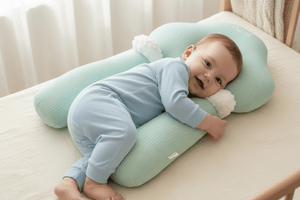 Baby lying on a green pillow with a soft toy, smiling.